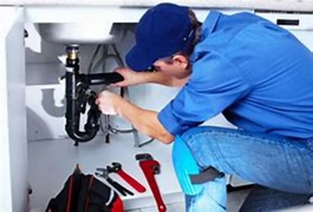 Image of a Plumbing Contractor working on a pipe under the kitchen sink